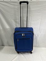 Full front view of the blue rolling luggage with extended handle, visible front zippered pockets and spinner wheels.
