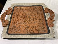 Top view of the ceramic rectangular platter featuring intricate black animal designs on a rust-colored center, speckled white border, and stylized animal-shaped handles.