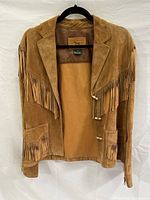 Front view of tan suede leather women's jacket with fringe on chest, arms, and pockets, hanging on black hanger.