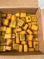 Box filled with yellow vintage composite mah-jongg tiles showing different traditional patterns including bamboo, circles, and Chinese characters.