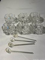 Wide shot of six crystal salt cellars arranged in two rows with five crystal spoons laid out in front, showing the full set and scale.
