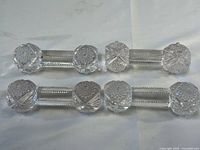 Four clear cut glass silverware rests placed side by side on a white surface, showing overall design and size.