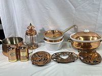 Full view of vintage hammered and polished copper kitchenware set including shakers, trivets, glass jar holder, saucepan, and large pot.