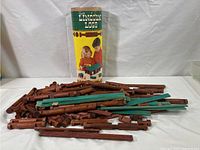 Wide shot showing many wooden Lincoln Logs pieces spread on a white background with original cylindrical packaging behind them.