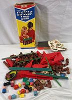 Photo of Lincoln Logs wooden pieces scattered with original colorful box standing upright showing children playing with the toy.