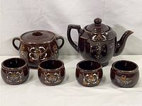 Full set showing large teapot, covered sugar bowl, bean pot, and four small cups decorated with colorful moriage floral motifs on dark brown glazed redware pottery.