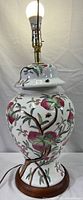Full view of vintage porcelain temple jar lamp showing painted botanical design and brass lamp fitting with bulb.
