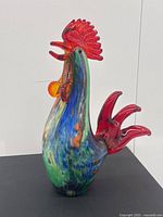 Full side view of the colorful art glass rooster showing its vibrant multicolor body and red translucent tail and comb.