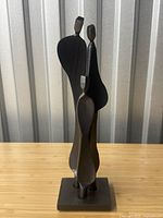 Front view showing three abstract elongated family figures with signed base