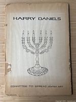 Portfolio front cover titled 'Harry Daniels' with menorah illustration and wear damage around edges.