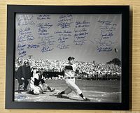 Front view of framed black and white photograph showing Babe Ruth mid-swing with multiple blue ink signatures