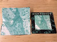 Photo of signed and inscribed front cover and signed cut album piece next to each other on wood surface.