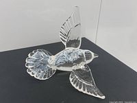 Clear glass bird figurine with wings and tail detailed, showing swirled white patterns inside and visible signature underneath on black background.