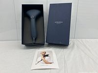 Dark grey handheld clothes steamer placed in a dark blue box with lid beside it, resting on fabric surface.