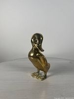 Front and side views of vintage solid brass duck figurine showing smooth polished surface, detailed feet and wings.