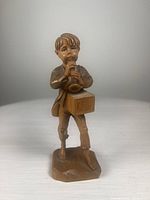 Front view of wood carved boy playing a horn with detailed facial features and clothing