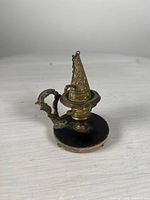 Front angle showing the ornate brass handle and conical snuffer attached by a chain on the lamp's round black base.