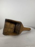 Top angled view of antique wooden scoop showing rectangular hollow, flat base, and open top.