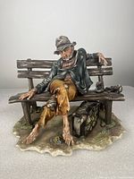 Front view of Capodimonte porcelain sculpture of a hobo sitting on a wooden bench, showing full figure, bench, and base.