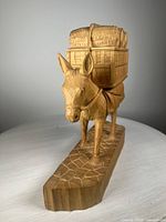Front angled view of wood carved donkey sculpture carrying barrels on a carved base, showing detailed wood texture and smooth finish.
