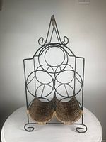 Front view of green steel wire and rattan bottle carrier with 5 circular bottle holders and scrollwork details