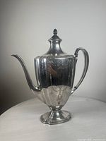 Front angle view of the vintage silver-plated Oneida Community coffee pot showing the decorative chased surface and curved spout.