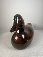 Front view of hand-carved wooden duck decoy showing smooth polished dark wood grain and glass eyes