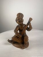 Front view of the wooden figurine showing the man holding the stringed instrument, smiling with detailed features and wearing a hat.