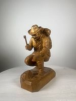 Front view of hand-carved wooden miner sculpture showing the figure crouching with hammer and detailed hat and clothing.
