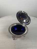 Front view of the open silver-plated mustard pot showing cobalt blue liner and detailed edges.
