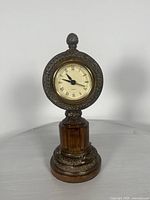 Clock front view showing ornate resin frame and wooden base with Roman numeral dial.