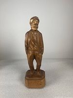 Front view of the wood carving showing full figure of a smiling man with hands in pockets and base signed 'Caron'.