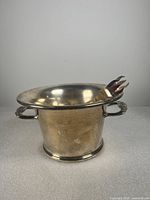 Front angle view of silver plated ice bucket and ice tongs on rim.