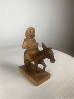 Photo showing front view of the hand-carved wooden figurine of Sancho Panza riding his donkey, placed on a white surface with clear lighting.