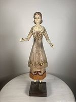 Front view of vintage folk art lady doll showing articulated arms, painted dress with floral motif, and wooden base stand.