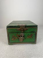 Front view of the green painted wooden jewelry box showing drawer with metal latch and floral butterfly decorations.