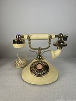 Side view of the vintage cream and gold rotary phone showing handset, base, and dial.