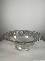 Front view of the vintage clear glass bowl showing delicate silver floral patterns along the scalloped rim and three-footed base.
