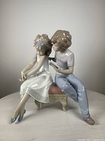 Front-side view of the figurine showing the two children sitting, with the girl looking downward and the boy appearing to read to her.