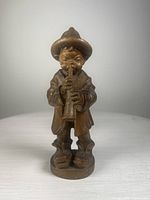 Front view of the wooden figurine showing the boy with a hat holding and playing a wind instrument.