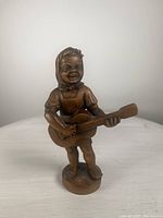 Front view of vintage wood carving figurine showing girl playing guitar with headscarf and dress.