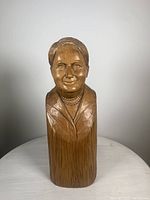 Front view of wooden bust sculpture depicting a smiling woman with necklace and jacket, standing about 13 inches tall.