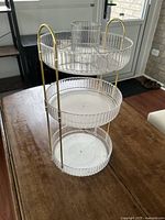 Front angle view of the 3-tier rotating organizer showing clear acrylic trays with ribbed edges and gold metal handles.