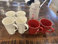Photo showing the 6 ceramic mugs in white and red colors along with the AeroPress box placed on a wooden table.