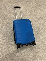 Blue Amazon Basics carry-on suitcase with extended handle resting on carpeted floor, showing exterior with spinner wheels.