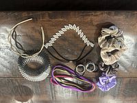 Top view of assorted hair accessories showing satin scrunchies, rhinestone and metal headbands, elastic and spiral hair ties, and silver-tone beaded accessories on a wooden surface.