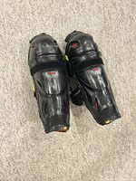 Pair of black and yellow Bauer hockey shin guards showing front hard shell with red and white Bauer logos and visible scuffs.