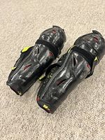 Pair of black Bauer youth hockey shin guards showing the hard plastic exterior with ventilation holes and some signs of wear.