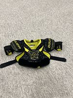 Front view of Bauer youth large ice hockey shoulder pads, showing black and yellow color, shoulder caps, chest padding, and adjustable straps.