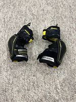 Pair of Bauer youth medium hockey elbow pads with black and yellow colors displayed on carpet, showing padding and straps